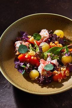 Top view of bowl with delicious crab salad with fresh vegetables and herbs placed on brown table