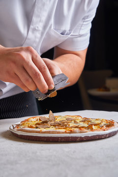 Unrecognizable cook slicing fresh truffle on tasty pizza while working in restaurant