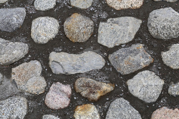 Road made of cobblestones and cement. Grey outdoor floor in a closeup from above. Sidewalk stones are asymmetrical and most of them have grey stones. Color image.