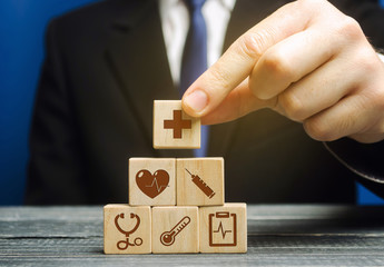 Businessman puts wooden blocks with the image of medical symbols. Healthcare and medical Insurance concept. Stethoscope, cross, thermometer and other. Medical care