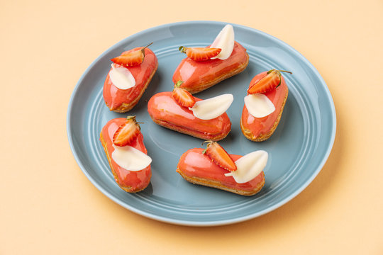 From above delicious eclairs with strawberry icing and white chocolate leaves placed on beige background