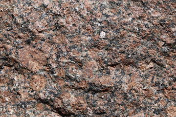Closeup of a big solid stone in red, orange and black tones. In this photo you can see the rustic texture of the uneven surface of the rock in detail. Perfect grungy background image. Color photo.