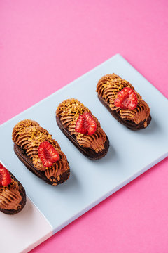 From above delectable chocolate eclairs with pieces of fresh raspberries and caramel cream placed in line on board on pink background