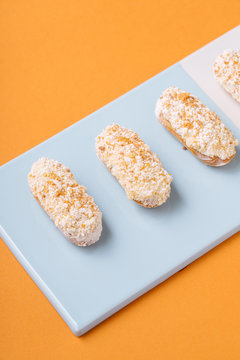 From above yummy soft eclairs with white creamy icing placed in line on board against orange background