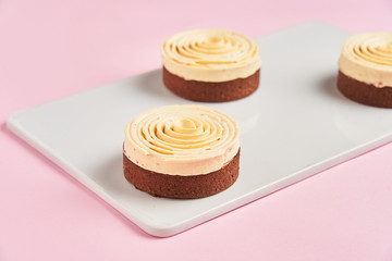 Closeup delicious chocolate pastry decorated with cream spiral and placed on board on pink background