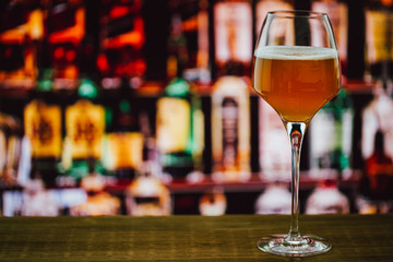 Beer in wineglass with foam in glass on wooden counter in bar on blur background