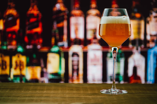 Beer in wineglass with foam in glass on wooden counter in bar on blur background
