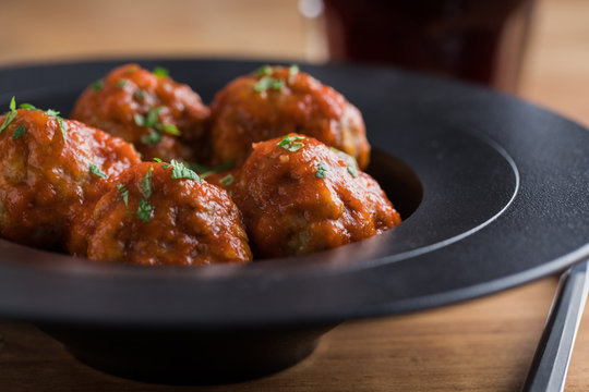 From above tasty cooked meatballs with tomato sauce serving with bread on black plate with cutlery and beverage on table