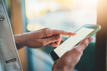 Closeup photo of female hands using cellphone device typing text message on touch screen, woman holding smartphone with blank screen with copy space for your text message or logo, flare light