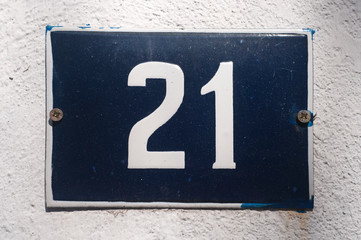 Weathered grunge square metal enameled plate of number of street address with number 21 closeup