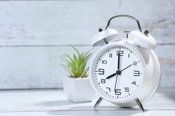 white retro alarm clock on the wooden table.  Green plant in a white pot.