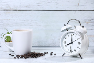 white retro alarm clock,  flowers cup of coffee , coffee beans and cinnamon on a wooden table....