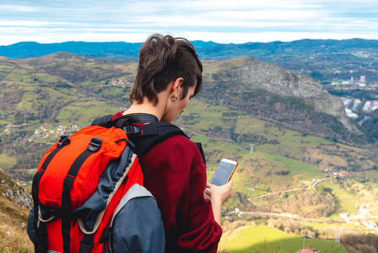 tourist with backpack and smartphone hiking on hill road under cloudy sky in Spain