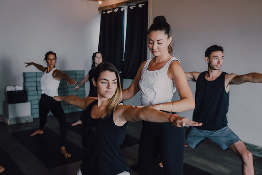 Smiling diligent female instructor in sportswear teaching warrior pose two group of sporty people doing exercise standing on sports mats in modern workout room