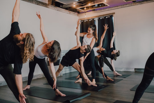 Smiling diligent female instructor in sportswear teaching revolved triangle pose to a group of sporty people doing exercise standing on sports mats in modern workout room