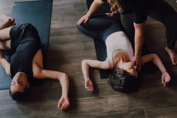 High angle of group of young sporty women and men in sportswear with eyes closed and legs crossed relaxing and deep breathing while lying in savasana position and meditating on sports mats in modern yoga studio