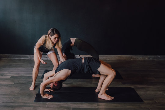 High angle of adult barefooted instructor in sportswear supporting man while teaching group of sporty people to do urdhva dhanurasana pose in contemporary workout room