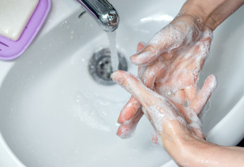 Woman washing hands with soap under the faucet in bathroom. Step by step picture instructions for thorough medical procedure. Step 6, wash between your fingers (inside).