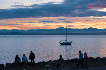 Silhouetted people on the Seattle waterfront at sunset with sailboat.