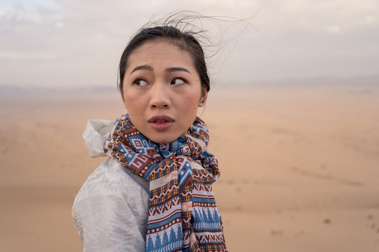 Side view of pensive young ethnic female tourist contemplating natural landscape while sitting on sandy dune in desert in Saudi Arabia looking away