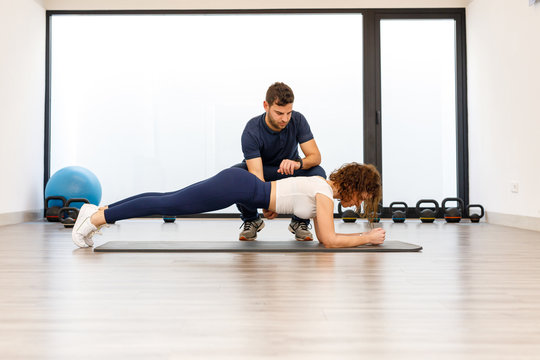 Side view of strong woman in plank position with male personal trainer in modern gym 