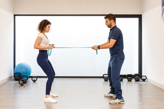 Side view of male and female athletes in active wear standing in front of each other and pulling elastic band in modern gym