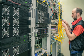A technician lays wires in the server room of a data center. The engineer connects the main...