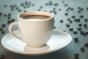 A Cup of coffee stands on a wooden table. Coffee beans scattered around