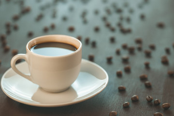 A Cup of coffee stands on a wooden table. Coffee beans scattered around