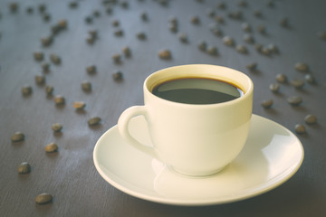 A Cup of coffee stands on a wooden table. Coffee beans scattered around