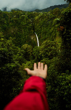 Unrecognizable person demonstrating wonderful waterfall in green rainforest on cloudy day in Costa Rica