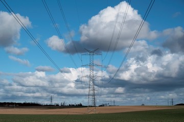 Field with electric poles and a beautiful blue sky with clouds highlighted by the sun