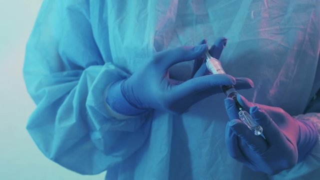 Infectious disease. Stationary treatment. Female doctor in protective gear filling syringe with drugs.