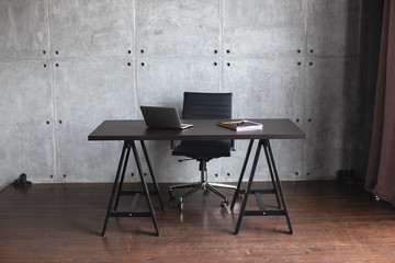 Desktop in the office. Dark concrete walls. Table with laptop and notebook. Office in modern style. 