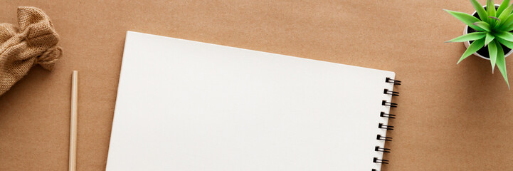 Brown background. View from above. Copy space with space for text. Mockup. Scattered coffee beans, open sketchbook, succulent and jute bag. Panorama