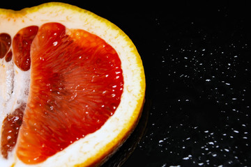 grapefruit pulp with drops of moisture on a black mirror