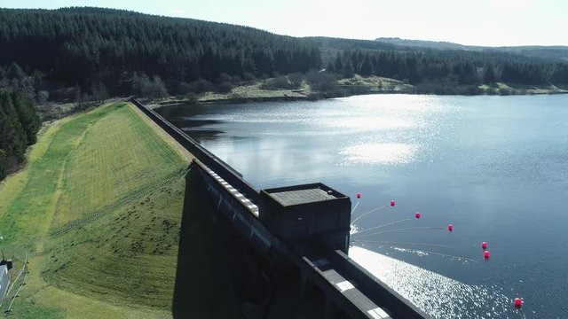 Low level aerial footage over a reservoir and dam revealing a scenic Scottish landscape on a bright Spring day.