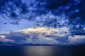 Naklejka na ściany i meble Panoramic view of ocean waters horizon line with dramatic cumulus thunderstorm cloudscape in blue sky background.