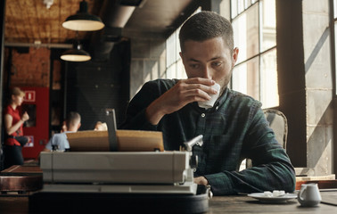 man writing on an old typewriter. In the meantime, he drinks coffee