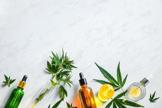 Various glass bottles with CBD oil, THC tincture and hemp leaves on a marble background. Flat lay, minimalism. Cosmetics CBD oil