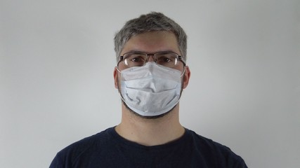 On the mans face are glasses and a medical mask. Portrait of a man. Dark clothes. Virus protection. Precautionary measures. Light background