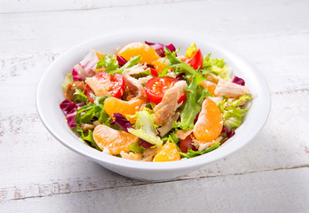 Salad with chicken, tangerines and vegetables in a bowl on an old white wooden table. Selected focus.