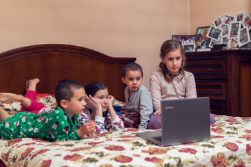 Pretty children looking at computer monitor while laying in bed and eating popcorn. Four young children watching cartoons or movies on a laptop. toned