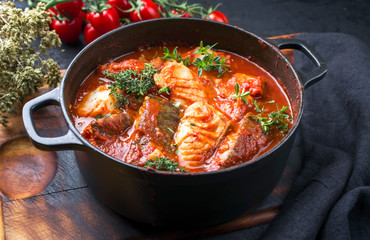 Traditional Brazilian fish stew moqueca baiana with fish filet in tomato sauce as closeup in a modern design cast-iron roasting dish - obrazy, fototapety, plakaty
