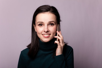 girl in a green turtleneck talking on the phone, portrait on a gray background