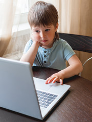 Curious toddler boy explores the laptop and presses buttons on computer keyboard.