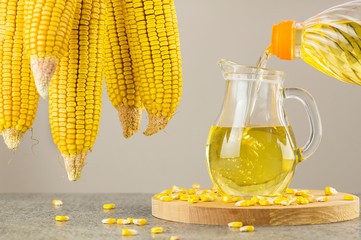 Pouring Corn oil in glass bottle with dried corn groats and kernels on rustic backdrop. Cooking oil composition