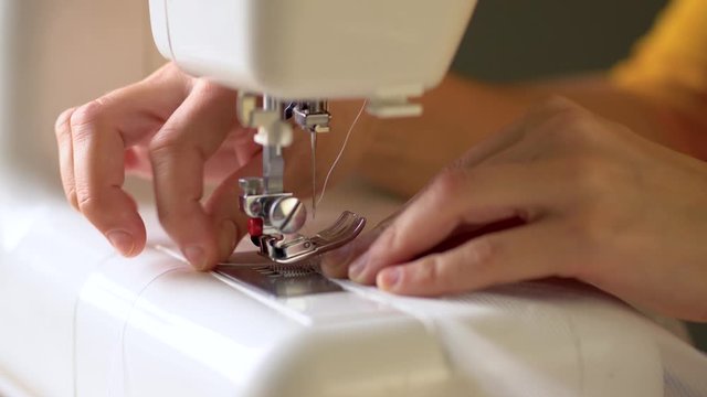 The process of hemming the edges of the curtains. The rolled edge of the fabric is brought under the presser foot of the sewing machine. The needle drops. The sewing process begins. Close up view.