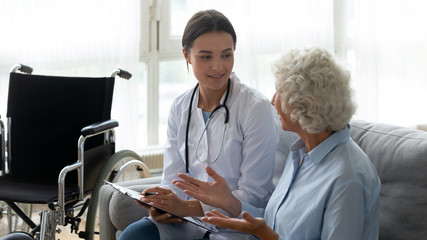 Supportive young woman doctor visit disabled senior grandmother consulting patient at home,...
