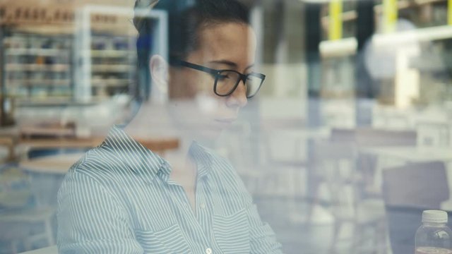 A woman in glasses filmed through the cafe window